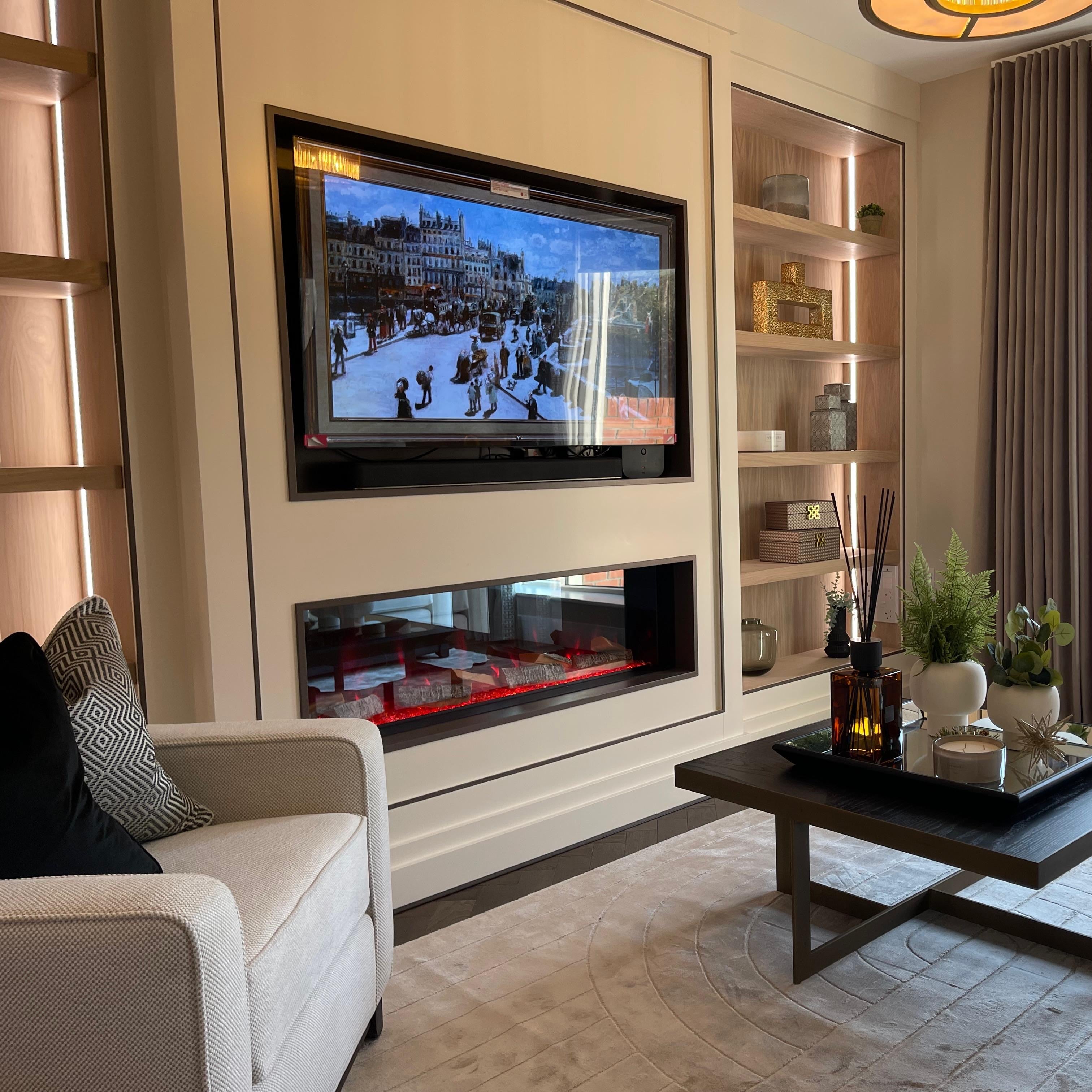 A modern living room interior featuring a large wall-mounted television above a built-in fireplace, with shelving, a dark wood coffee table, and a large window with curtains.