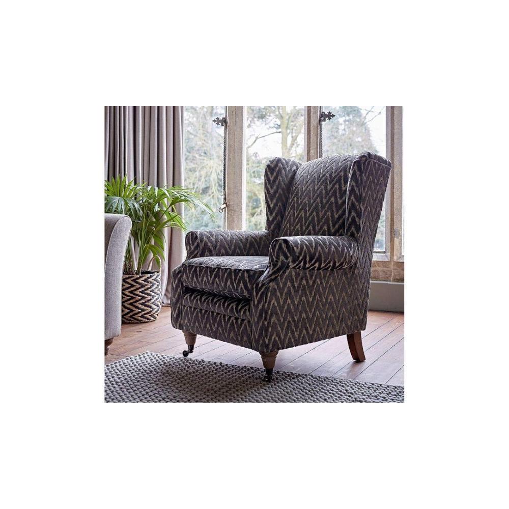Heather Bespoke Wing Chair in dark patterned fabric, with wooden feet and casters, on a rug.