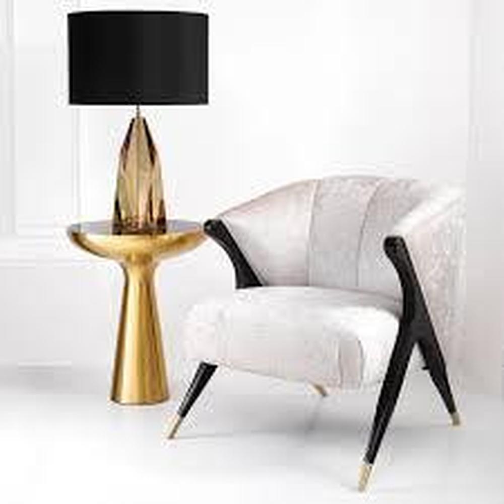 Pavone Occasional Armchair in off-white velvet with black and brass finish legs, beside a gold table lamp.