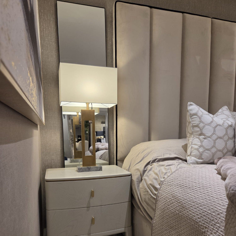 Custom Belle bed with a tall upholstered panel headboard, beige bedding, and a matching nightstand with lamp.